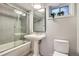 Cozy bathroom featuring a pedestal sink, a tub/shower combo with glass doors, and a window for natural light at 814 S High St, Denver, CO 80209