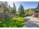 Beautiful backyard with stone retaining wall, green lawn, mature trees, and adjacent road at 11531 S Deer Creek Rd, Littleton, CO 80127