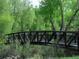 A metal bridge crosses a stream surrounded by lush green trees and vegetation at 10151 W 38Th Ave, Wheat Ridge, CO 80033