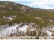 An aerial view shows the wooded acreage on a snow-covered lot with mountain views, featuring a winding driveway to the house at 9239 Black Mountain Dr, Conifer, CO 80433