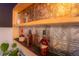 Detailed shot of a modern wet bar showcasing textured metal backsplash, wooden shelving, and an assortment of liquor bottles at 2548 S Zurich Ct, Denver, CO 80219