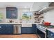 Stylish kitchen featuring blue cabinetry, stainless steel appliances, floating shelves, and a farmhouse sink at 8445 Lamar Dr, Arvada, CO 80003