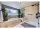 Bright bathroom featuring a soaking tub, glass-enclosed shower, light tile, and various potted plants at 2522 W Dry Creek Ct, Littleton, CO 80120