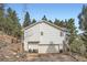 View of the exterior of the house showing a multi-car garage, steps up to a side entrance, and wooded surrounding at 13495 Shiloh Rd, Conifer, CO 80433
