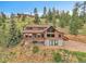 A wide exterior shot of a log cabin home that includes a deck, garage, and staircase at 25704 Shiloh, Conifer, CO 80433