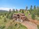 An expansive exterior view showcasing a beautiful cabin-style home nestled among lush greenery and trees at 25704 Shiloh, Conifer, CO 80433