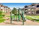 Community playground with a green metal slide and a green metal ladder surrounded by lush greenery and apartment buildings at 7440 S Blackhawk St # 4-104, Englewood, CO 80112