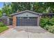 Attached garage with a concrete driveway, gray door, and brick accents surrounded by lush greenery at 4634 W Tufts Cir, Denver, CO 80236