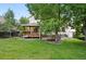 Landscaped backyard featuring a spacious lawn, mature trees, and a wooden deck at 4674 Winona Pl, Broomfield, CO 80020