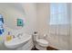 Well-lit half bathroom with pedestal sink, toilet, and window with sheer curtains at 6335 E 143Rd Dr, Thornton, CO 80602