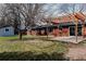 A pergola covered concrete patio connects a brick house and a quaint blue storage shed in the backyard at 3400 Moore St, Wheat Ridge, CO 80033