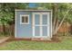 Backyard storage shed with white doors and a window surrounded by lush greenery at 3224 S Dudley St, Lakewood, CO 80227
