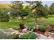 A tiered backyard features a lush lawn, mature trees, and flowering bushes and stone walkways at 5904 Meadowbrook Dr, Morrison, CO 80465