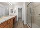 Bathroom area featuring dual sinks, wooden vanity, large mirror, walk-in shower and wood-look flooring at 7713 S Zante Ct, Aurora, CO 80016