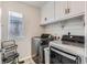 Bright laundry room with stainless steel washer, dryer, white cabinets, and a window at 18809 E 66Th Ave, Denver, CO 80249