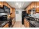 Galley kitchen with wooden cabinets, black appliances, granite countertops, and tile flooring at 8600 E Alameda Ave # 21-208, Denver, CO 80247