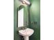 Stylish powder room featuring a pedestal sink with gold accents, arched mirror, and green walls at 10222 Gemstone Ct, Parker, CO 80134