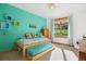 Cozy bedroom with a vibrant accent wall, a trundle bed, a wooden dresser, and a sun-filled window with curtains at 4305 Easley Rd, Golden, CO 80403