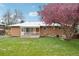 Brick home backyard featuring a small patio and a vibrant, large pink blossoming tree at 8307 E Lehigh Dr, Denver, CO 80237