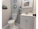 A half bathroom features a toilet, vanity with sink, decorative wall hangings, and light gray walls at 16301 Hudson Rd, Hudson, CO 80642