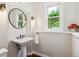 Bathroom featuring a pedestal sink, round mirror, vanity lighting, and window at 20496 Stonewood Trl, Morrison, CO 80465