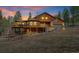 Two-story wood home with a deck, garage, and lush surrounding trees under a stunning sunset sky at 9590 S Warhawk Rd, Conifer, CO 80433