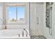 Bright bathroom featuring a soaking tub, glass shower and a window overlooking a view of the exterior at 12551 W 84Th Cir, Arvada, CO 80005