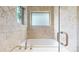 Elegant bathtub with travertine tile surround, a clear glass shower door, and natural light at 1426 S Pearl St, Denver, CO 80210