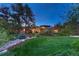 Well-manicured front yard at dusk featuring lush green grass, mature trees, and landscape lighting at 2597 Oak Vista Ct, Castle Rock, CO 80104