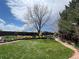 Landscaped backyard featuring a mature tree, flowerbeds, green grass, a wooden fence, and a brick pathway at 12408 W 83Rd Ave, Arvada, CO 80005