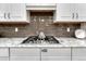 Close-up of the kitchen cooktop, featuring stainless steel appliances and gray tiled backsplash at 3242 Waterfront Dr, Monument, CO 80132