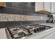 Close up of a gas stove with black backsplash and tiled accent in a bright, modern kitchen at 19409 W 88Th Dr, Arvada, CO 80007