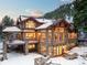 Majestic multi-story mountain home featuring large windows, stone accents, snow-covered roof, and outdoor deck at 6169 Flat Creek Dr, Evergreen, CO 80439