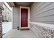 Inviting covered front porch featuring a red front door and brick detailing at 5152 Bittercress Rd, Brighton, CO 80640