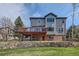 Expansive exterior view showing a multi-story home, deck, stone retaining wall, and well-maintained lawn at 7411 S Curtice Ct, Littleton, CO 80120