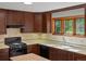A cozy kitchen features dark wood cabinets, a black gas range, and a large window with views of lush greenery at 11824 E Basswood Ln, Franktown, CO 80116