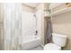 Bathroom with white tile shower, decorative curtain, open shelves, and standard toilet at 2480 W Jamison Way, Littleton, CO 80120