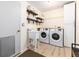 Well-lit laundry room with a utility sink, open shelving, newer washer and dryer, and storage cabinet at 2480 W Jamison Way, Littleton, CO 80120