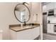 A well-lit bathroom featuring a round mirror, modern vanity, and a peek into an adjoining kitchen at 2120 N Downing St # 216, Denver, CO 80205
