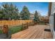 Wooden deck and fenced backyard with lush grass and mature trees on a sunny day at 23955 Glenmoor Way, Parker, CO 80138