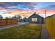 The fenced backyard features a manicured lawn and a detached garage under a colorful sunset sky at 469 S Perry St, Denver, CO 80219