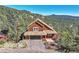 Aerial view of a mountain home featuring a two-car garage and mature trees surrounding the property at 31324 Kings Vly, Conifer, CO 80433