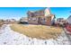 A spacious backyard featuring a grass lawn, partial snow cover, and patio area at 9335 Dunraven Loop, Arvada, CO 80007
