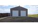 Exterior of a gray detached garage with two white garage doors and a well-kept lawn at 11595 Pass Me By Rd, Strasburg, CO 80136