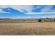 A vast field with a blue sky horizon and a scattering of bare trees and distant houses at 2840 Wagner St, Strasburg, CO 80136