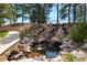 Scenic waterfall feature with natural stone, lush greenery, and a tranquil pond at 8417 High Ridge Ct, Castle Pines, CO 80108