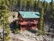 Cozy two-story cabin with a green roof nestled among trees, featuring a spacious deck for outdoor enjoyment at 451 Harris Dr, Idaho Springs, CO 80452