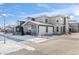 View of modern townhome with white two-car garage and stone facade in snow-covered Colorado at 350 High Point Dr # C201, Longmont, CO 80504
