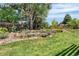 Beautiful backyard featuring a stone retaining wall, mature trees, grassy area, and landscaping at 5185 W Fair Pl, Littleton, CO 80123