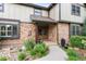 Inviting entrance featuring a tiled porch, brick facade, manicured garden, and a wooden front door at 5185 W Fair Pl, Littleton, CO 80123